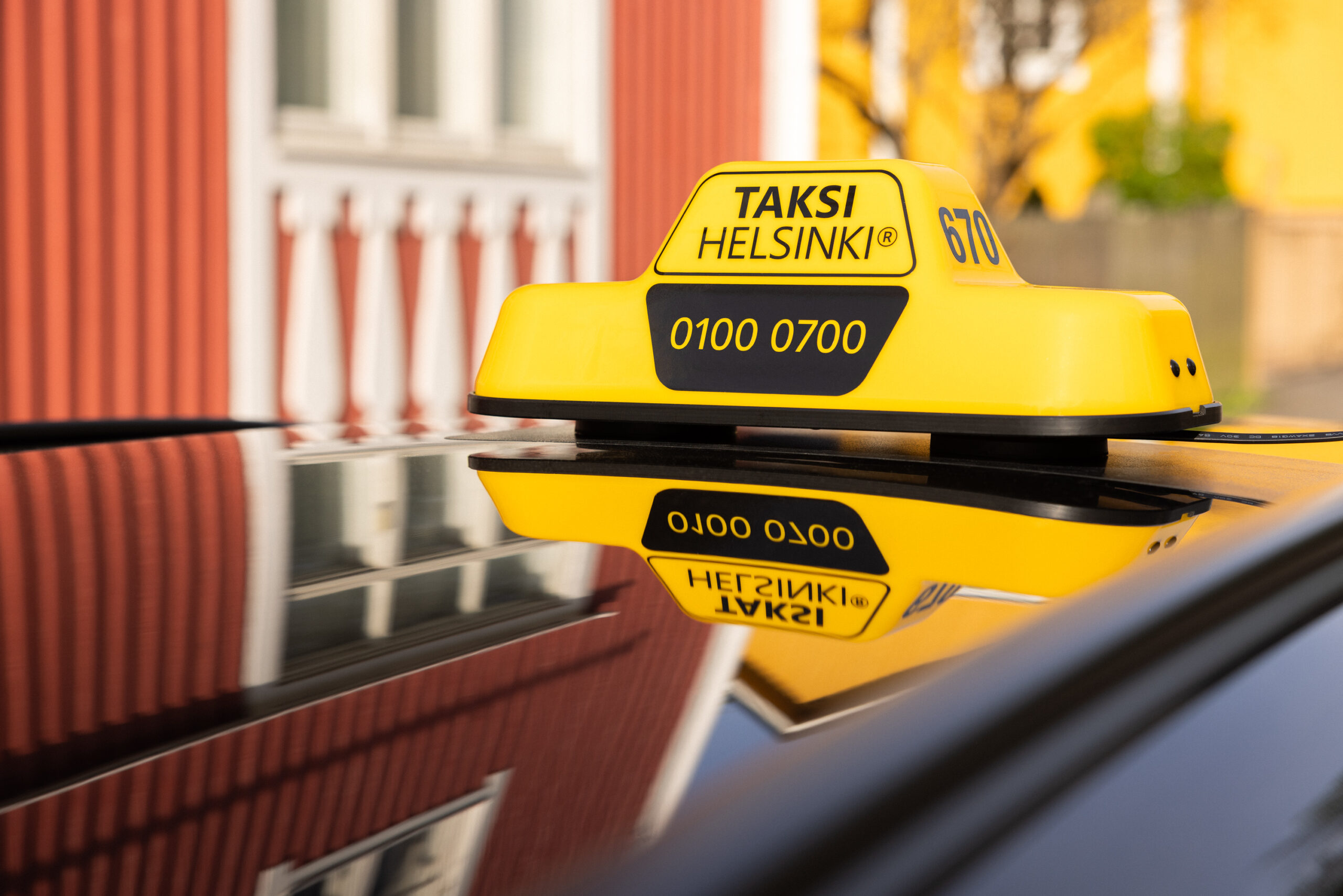 The Taksi Helsinki taxi sign on the car roof, with colorful buildings in the background.